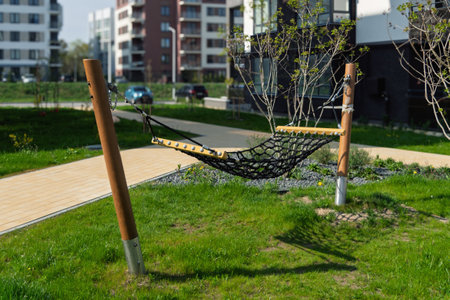 Net hammock stretches between sturdy wooden posts on fresh green grass in a modern courtyard, inviting relaxation and outdoor enjoyment.の写真素材