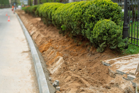 New curb lines a freshly dug roadside with green bushes, highlighting urban landscaping, street renovation, and city improvement work.の写真素材