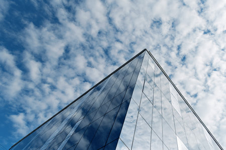 Sharp corner of a modern glass building rises dramatically towards the sky, reflecting dynamic clouds and creating a sense of endless space and innovation.の写真素材