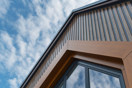 Low angle of contemporary wooden facade with geometric lines and wide glass windows reflecting the sky, highlighting modern architectural beauty.の写真素材
