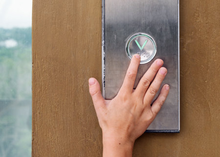 Child's hand presses elevator down button on metal panel, capturing the moment of independence, curiosity, and urban daily life experience.の写真素材