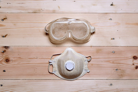 Protective goggles and dust mask lie on wooden floor, highlighting essential safety measures during...