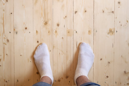 Person in white socks stands on warm light wooden floor with tactile grain and knots, highlighting...