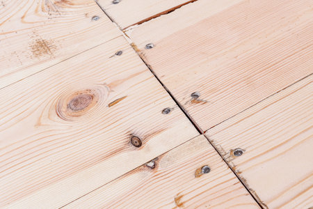 Natural wooden floorboards with visible knots, cracks, and gaps reveal need for repair, renovation, or protection in a cozy home interior.の写真素材