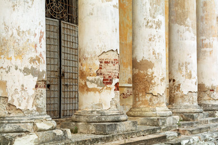 Weathered stone columns with peeling paint and exposed brick reveal the faded grandeur of an...