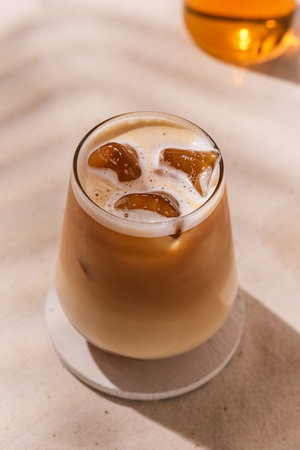 Chilled autumn latte in a stylish glass with ice cubes and creamy froth glows in warm sunlight,...