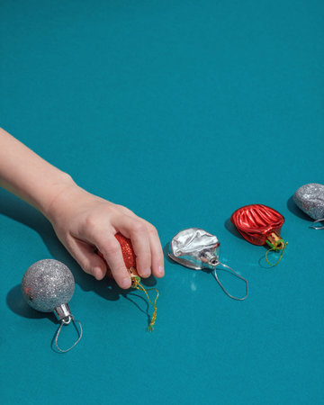 Child hand picks Christmas ornament from row of intact baubles on teal.