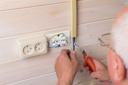 Close-up of man stripping insulation from electrical wire with pliers during socket installation,...