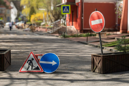 Traffic signs and barriers block empty city street during road construction under spring sunlightの写真素材