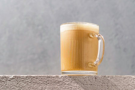 Warm latte in ribbed glass mug on textured concrete surface, wide gray background keeps minimal style and copy space for design.の写真素材