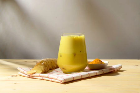 Iced turmeric ginger latte in modern glass with ice cubes stands on towel with spices, cool bright...