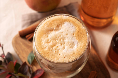 Cozy maple apple latte in clear glass on wooden board with cinnamon sticks and warm autumn light creates relaxed seasonal moodの写真素材