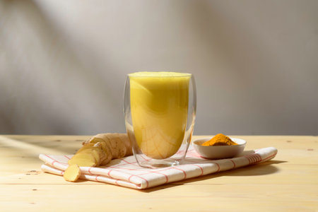 Warm turmeric ginger latte in double wall glass sits on checked towel with spices, inviting slow mindful wellness morning ritualの写真素材