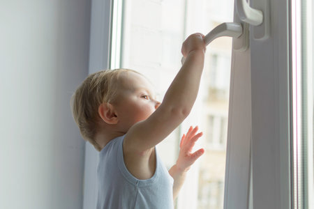 Toddler reaches up to window handle indoors, clearly showing home safety issue and need of protection from child falling out.の写真素材