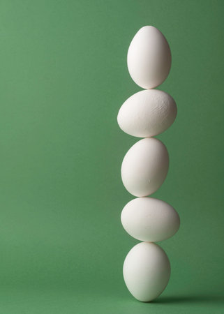Five white eggs balancing in a vertical line on green background forming clean minimal concept of fragile stability and precise harmonyの写真素材