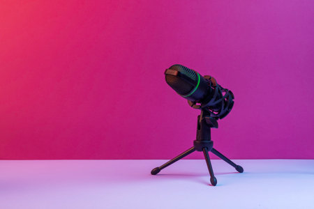 Studio microphone on tripod stands against vibrant pink backdrop forming clean modern setup for podcasts, streaming and audio contentの写真素材