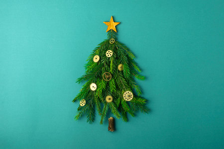A stylized Christmas tree made of fresh evergreen branches and golden gears forms a creative holiday scene on a textured teal background.の写真素材
