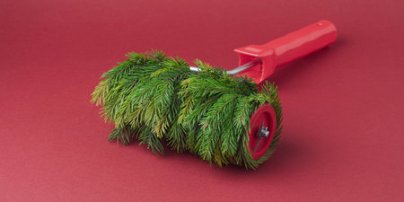 Fir-wrapped paint roller resting on deep red surface presents bold creative Christmas concept with rich natural textureの写真素材