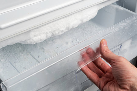 Hand opens freezer drawer with heavy ice buildup on evaporator, illustrating need for manual defrost and regular appliance maintenanceの写真素材