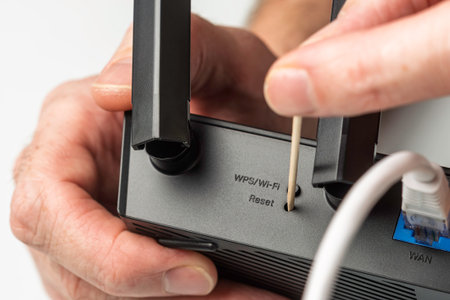 Closeup of hand resetting WiFi router with toothpick through WPS reset hole during internet connection troubleshooting at homeの写真素材