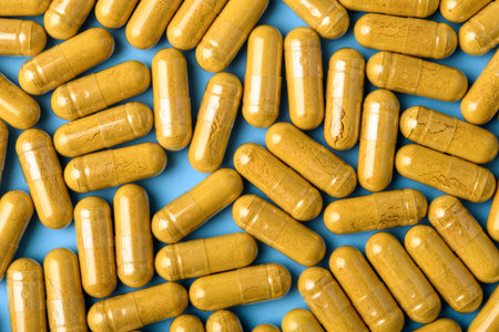 Yellow herbal capsules form dense pattern on blue background, macro texture for vitamin packaging,...