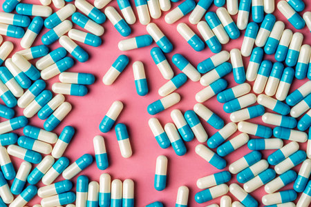 Blue and white capsules frame pink background with central copy space, modern healthcare layout for...
