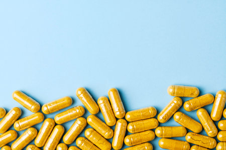 Yellow herbal capsules form border on pastel blue background, clean wellness concept with wide copy space for supplement advertising.の写真素材