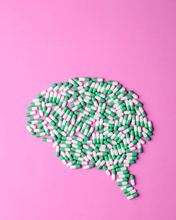 Green and white capsules form brain silhouette on pink background for mental health, pharmacy...