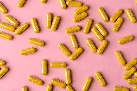 Yellow turmeric supplement capsules spread across pink background, bright flat lay with copy space for health promotion.の写真素材