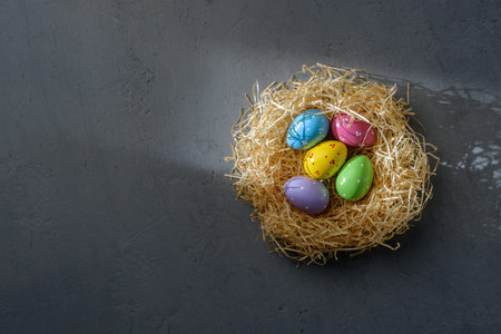 Bright Easter eggs in straw nest on dark gray concrete glow in sunbeam, strong shadow and copy space...