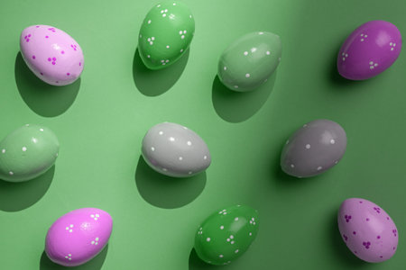 Colorful painted Easter eggs with dot patterns cast strong shadows on green background, modern flat...