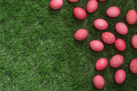 Red dyed Easter eggs rest on lush green grass with generous copy space, creating fresh spring...