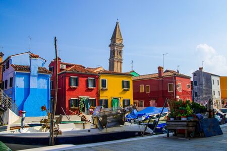 Colorful houses, boats, potted plants, leaning bell tower under the brilliant italian sky.の写真素材