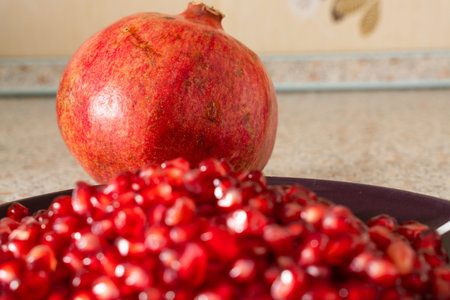 red ripe pomegranate seeds on a plate close-up. the fruit of pomegranate on a table with a marble...