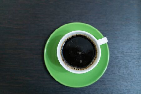 Cup of black coffee on a green saucer on a wooden table close-upの写真素材