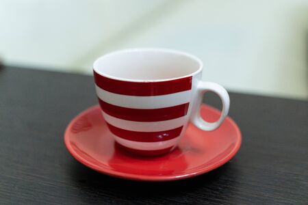 Cup with red and white stripes on a red saucer on a wooden tableの写真素材