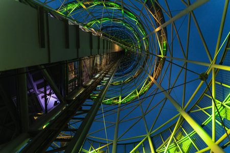 abstract metal design of the tower with green neon lights at night, the view from below