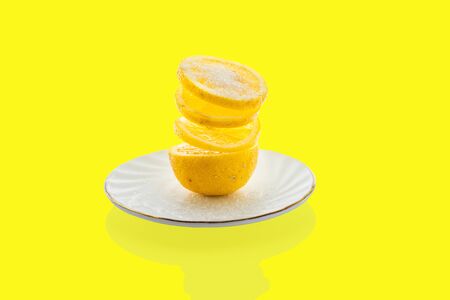 a fresh yellow lemon on a plate casts a shadow on the table on a light yellow backgroundの写真素材