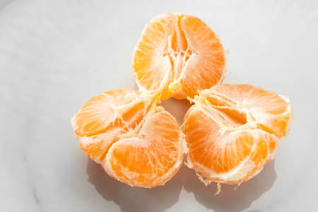 peeled tangerine with slices on a white plate close-up on a white backgroundの写真素材
