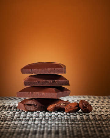 pieces of milk chocolate and coffee beans on an orange gradient background and a place for textの写真素材