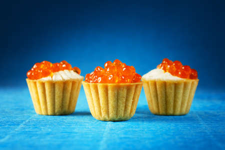 three tortalettes with red caviar on a blue background close-upの写真素材