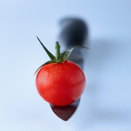 red cherry tomato on a knife blade on a light backgroundの写真素材