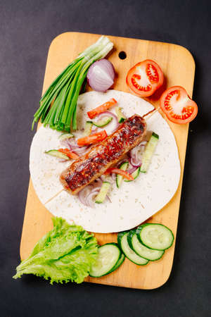 Grilled lula kebab on pita bread with vegetables on a dark backgroundの写真素材