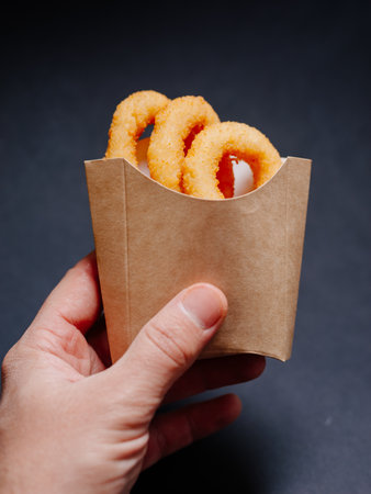 A man's hand holds a paper box without logo with fried onion rings.の写真素材