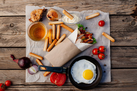 Fast food. Eastern food. Shish kebab, lyulya-kebab, shaverma, pita gyros, shawarma. Street food. Shaurma is on the wooden table, fried egg and beer. Fried eggs in a frying pan.の写真素材