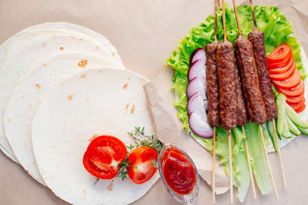 Fast food. Eastern food. Shish kebab, lyulya-kebab, shaverma, pita gyros. Dishes of oriental cuisine lying on pita bread and decorated with greens and vegetables, sauces and French fries.の写真素材