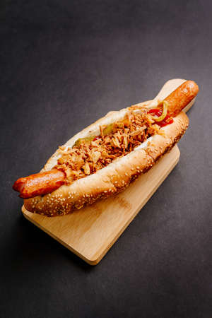 Danish hot dog with fried sausage, ketchup, mustard sauce and raw and fried onions isolated on black backgroundの写真素材