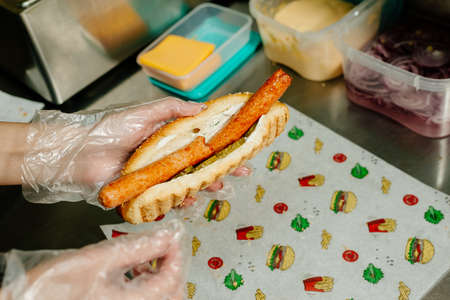 Danish hot dog. the process of preparing a Danish hot dog in the kitchen in a diner. Danish hot dog with fried sausage, ketchup, mustard sauce and raw and fried onionsの写真素材