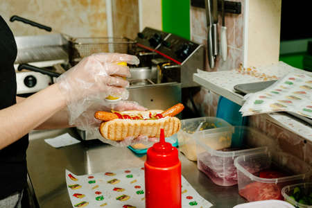 Danish hot dog. the process of preparing a Danish hot dog in the kitchen in a diner. Danish hot dog with fried sausage, ketchup, mustard sauce and raw and fried onionsの写真素材