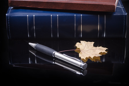 two albums in a blue and brown cover, pen and maple leaf lie on a black glossy surfaceの写真素材